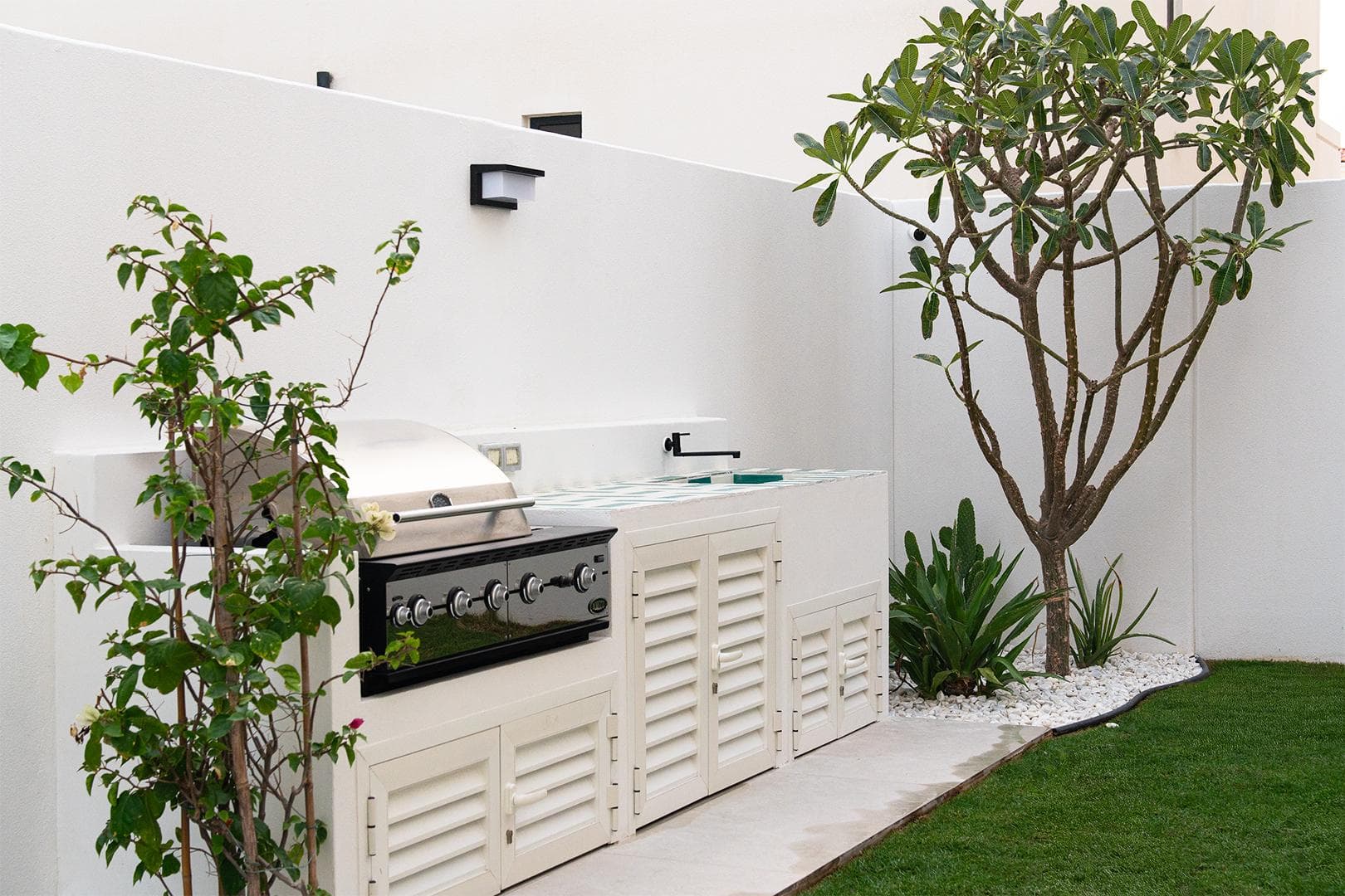 Outdoor kitchen with louvered cabinetry, barbecue grill and frangipani tree