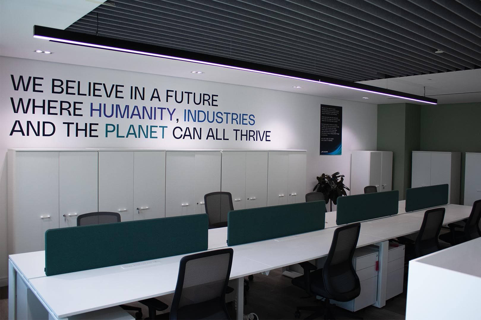Maire Tecnimont open-plan office with brand mural and acoustic baffle ceiling