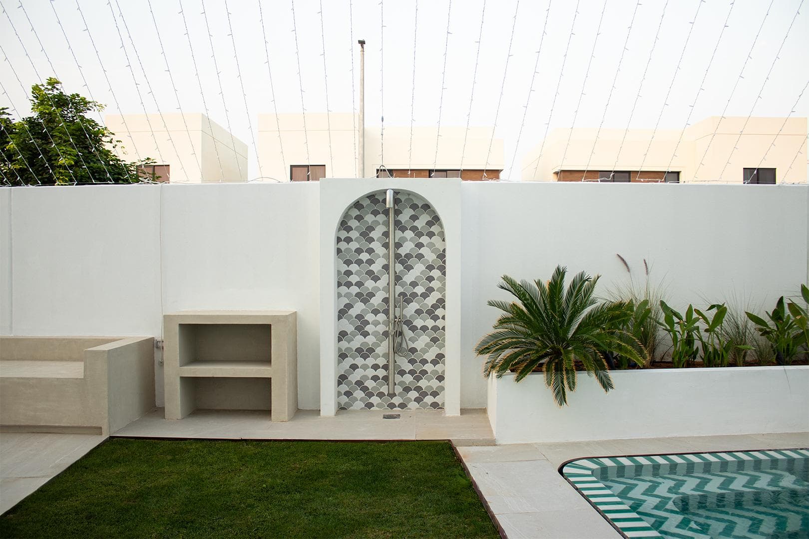 Arched outdoor shower in fish-scale tile beside a chevron-tiled pool