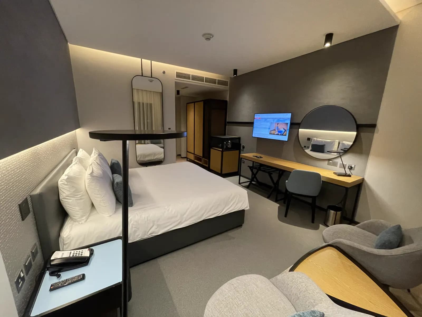 Hotel room with work desk, round mirror and integrated bedside joinery