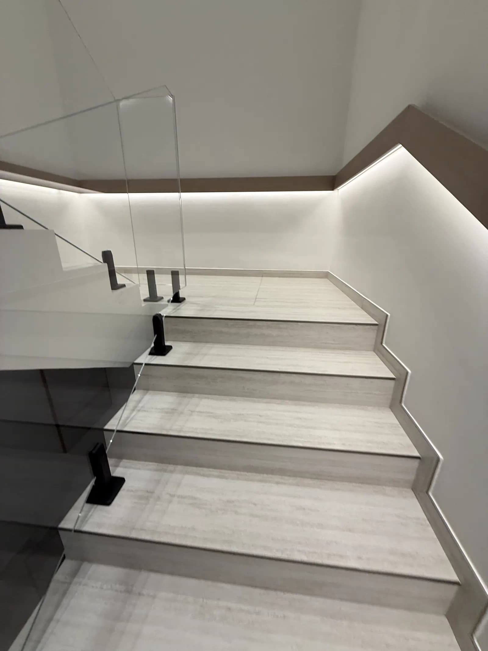 Stone staircase with a frameless glass balustrade and concealed cove lighting