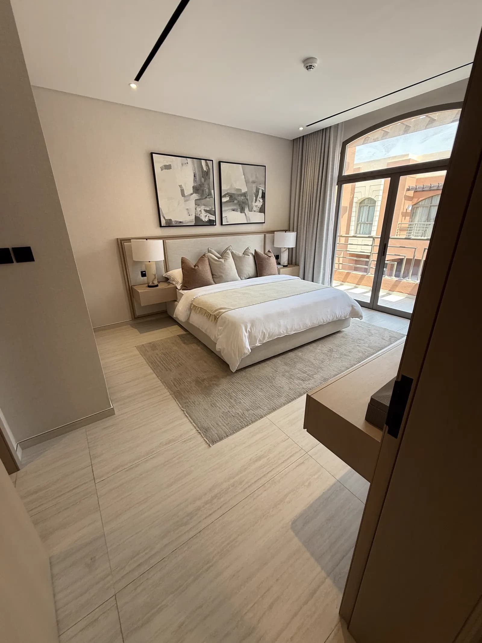 Bedroom with upholstered headboard wall, framed artwork and arched window