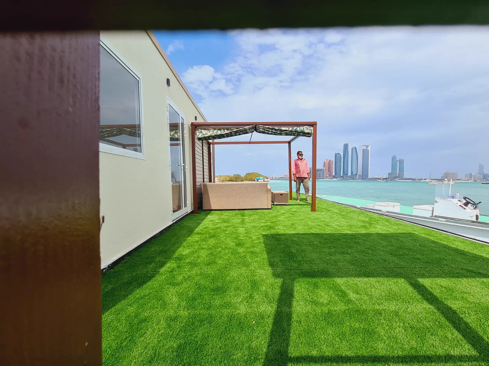 Rooftop garden with lawn and a timber pergola overlooking the Abu Dhabi skyline