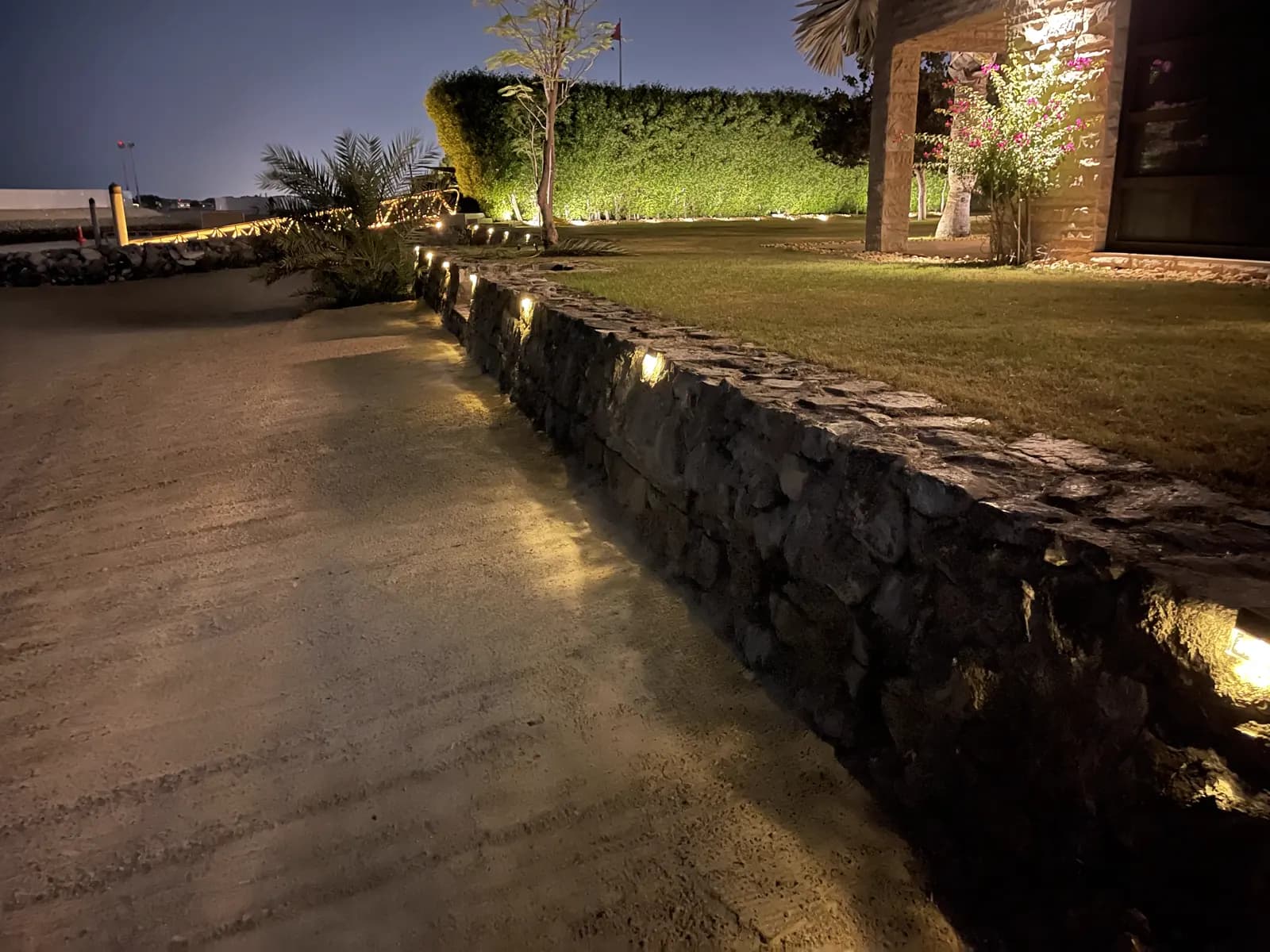 Illuminated stone boundary wall and lawn in a villa garden after dark