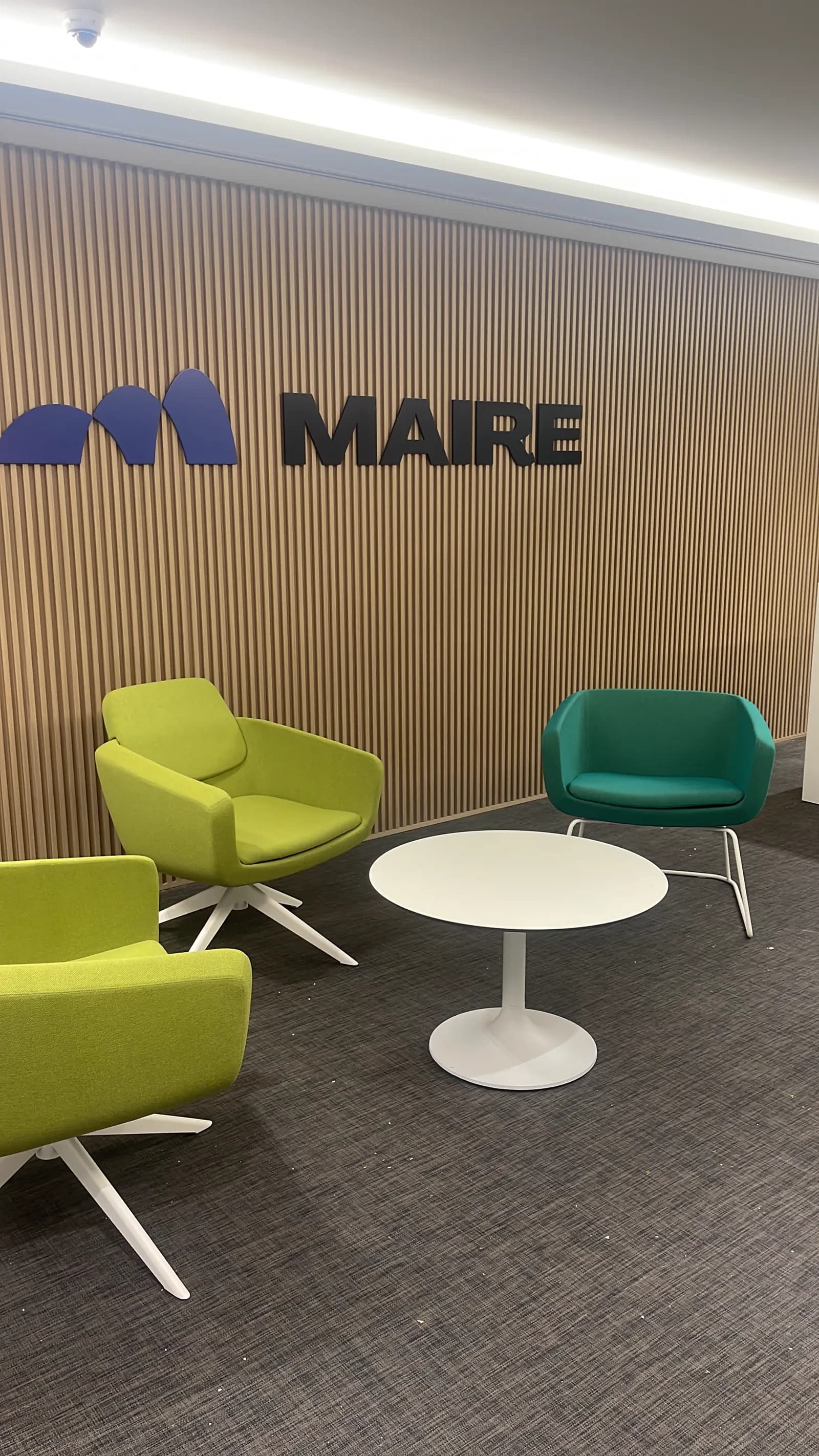 Maire Tecnimont waiting lounge with green and teal armchairs against a timber slat wall