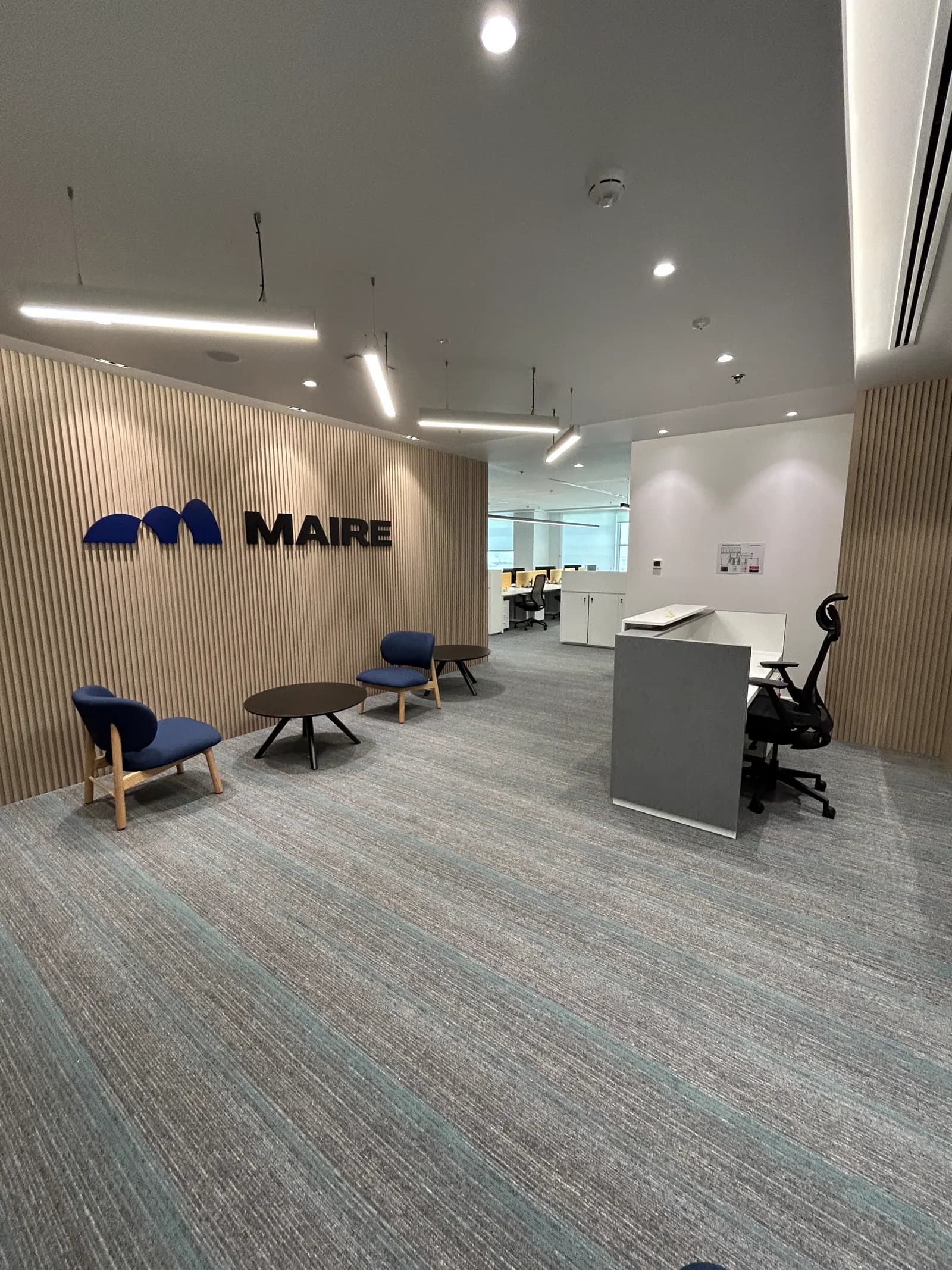 Maire Tecnimont reception lounge with brand wall, blue seating and linear lighting