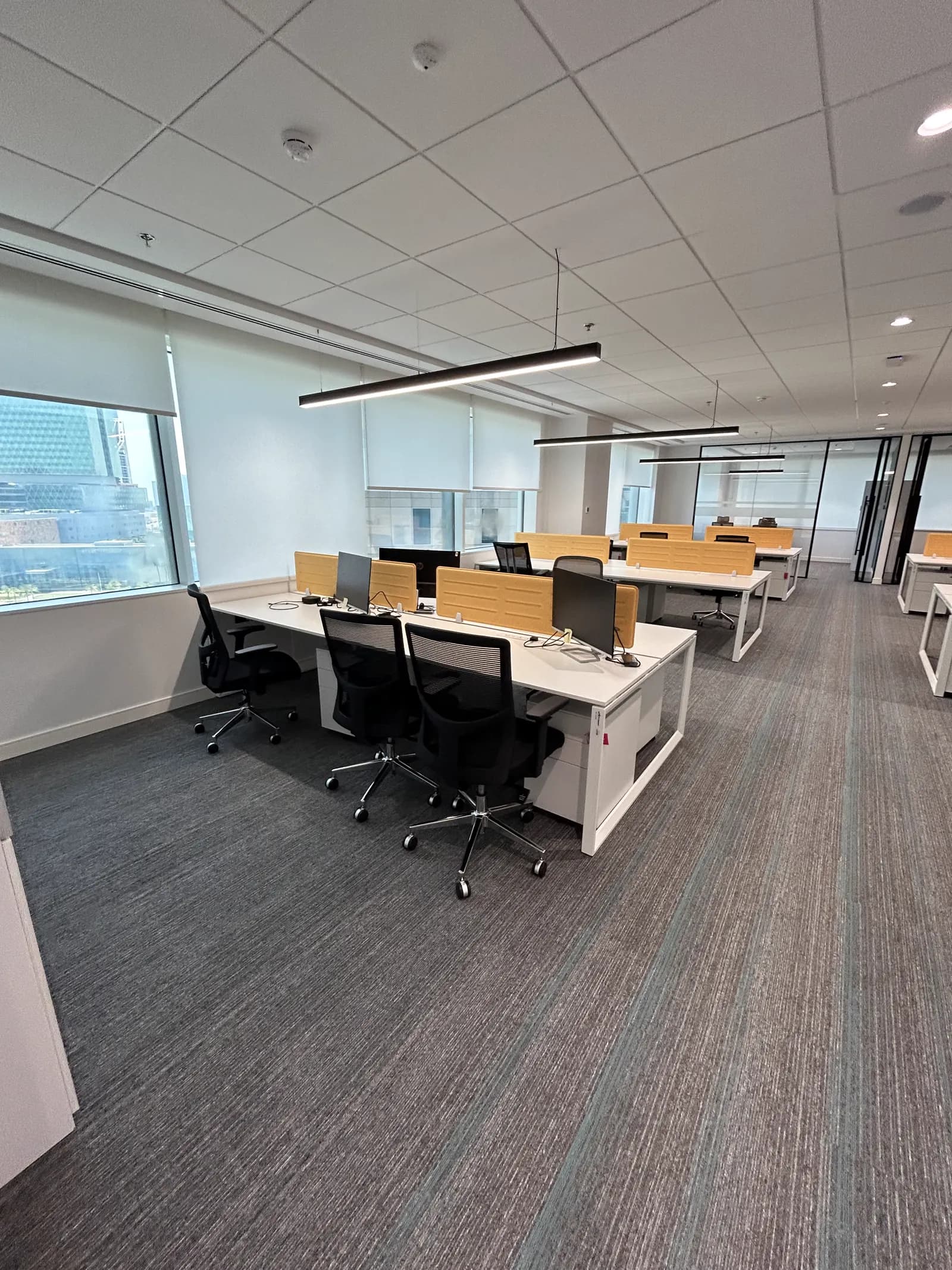 Desk pods with linear pendant lighting along a glazed office facade