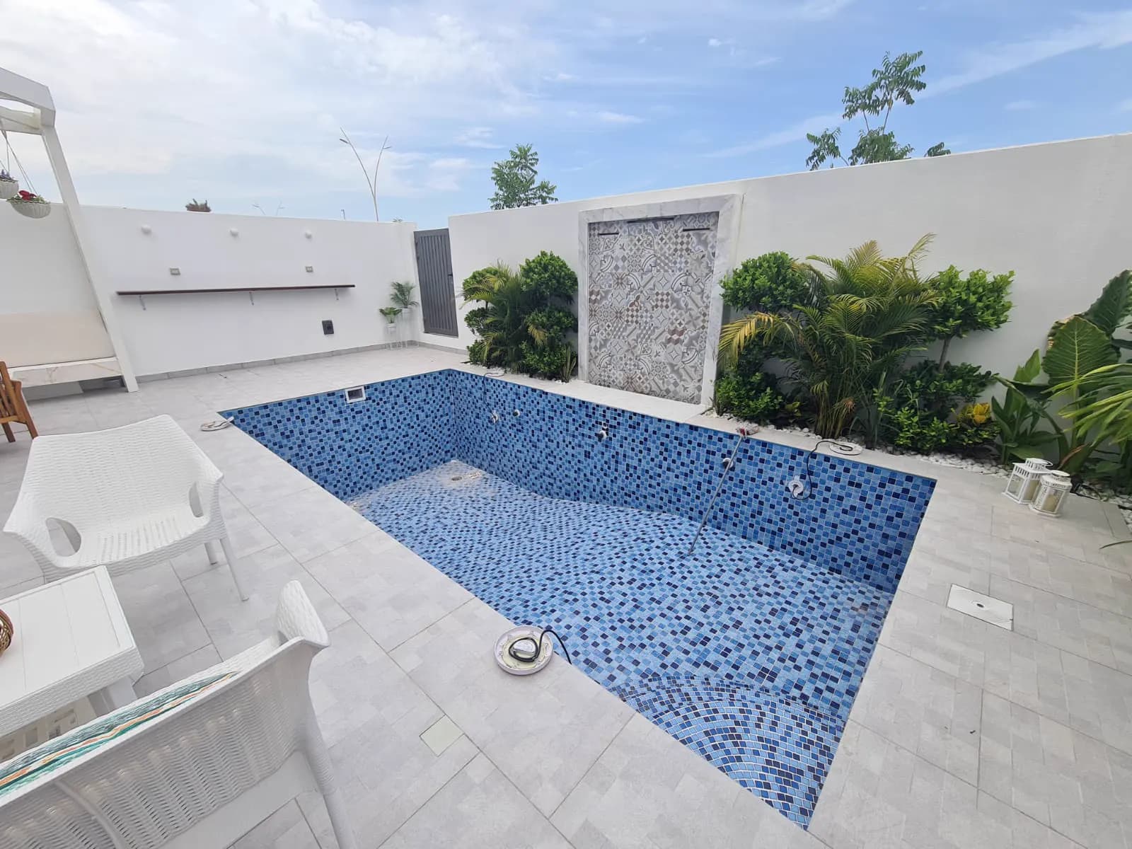 Blue mosaic-tiled pool in a walled courtyard with a carved stone feature panel and planting