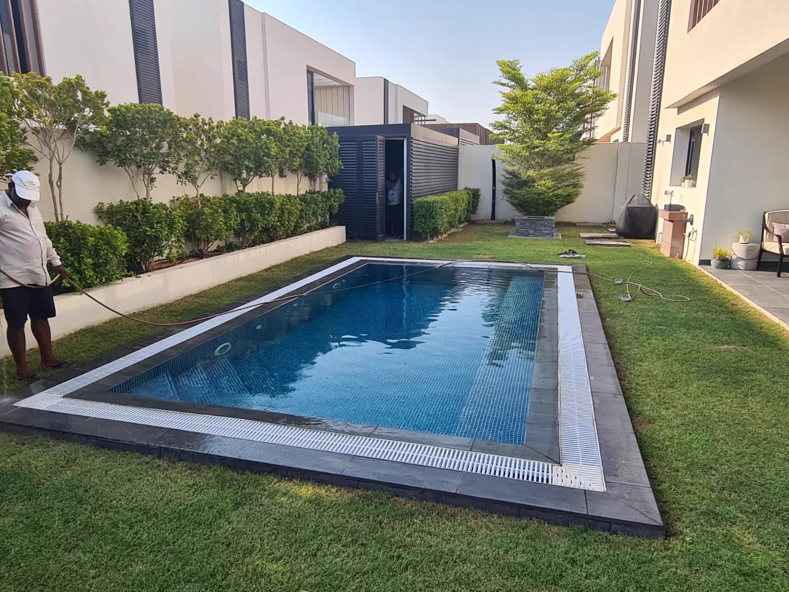 Pool with a stone coping set into a lawn, framed by a clipped hedge and villa wall