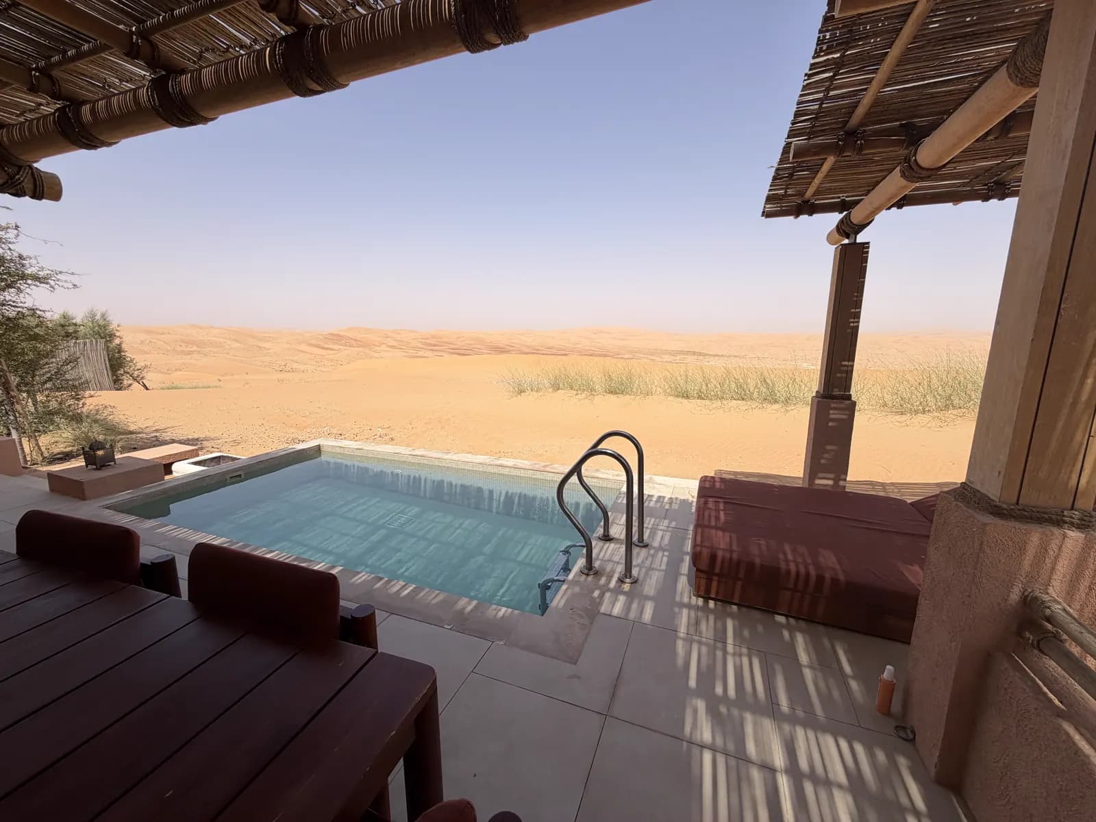 Pool and hardwood deck under a palm-thatch shade structure looking out over open desert